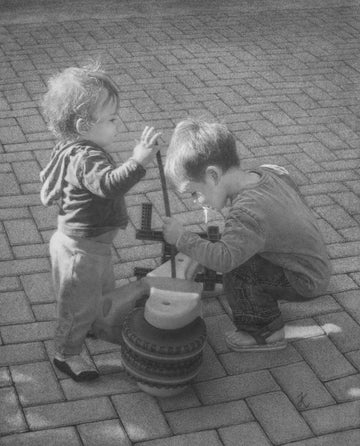BOYS POKING A BALANCE BIKE WITH A PLASTIC STICK